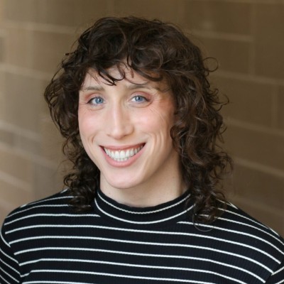 Quinn smiling in a black and white striped shirt against a brick wall