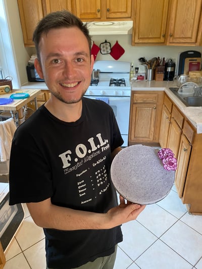 Ben holding a purple cheezecake he made in his black FOIL t-shirt