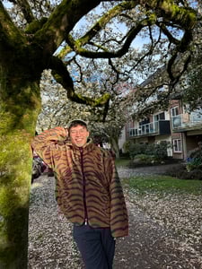 Peter in a tiger striped fluffy sweater, smiling and leaning on a mossy tree